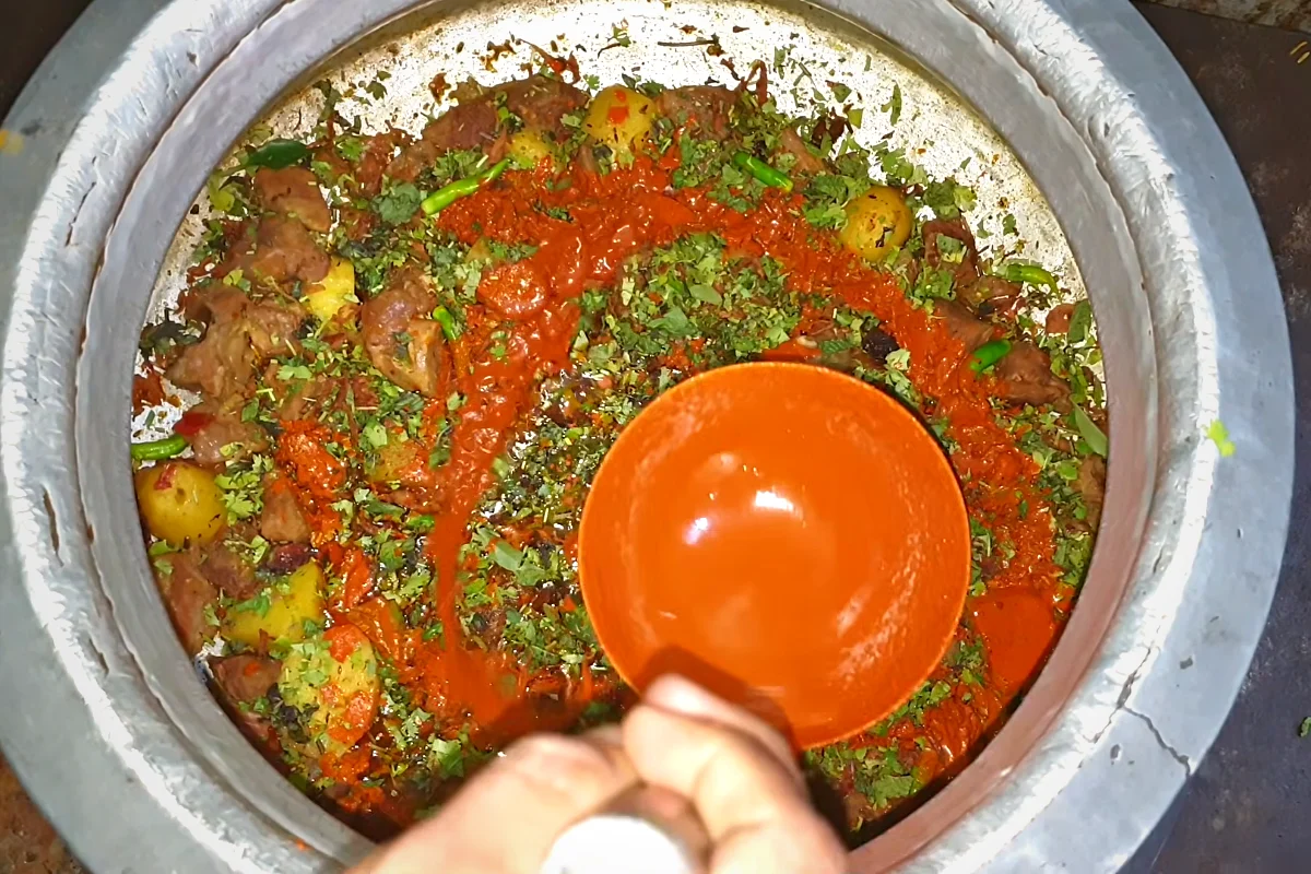 Green herbs and orange food colour spread over beef korma before adding rice