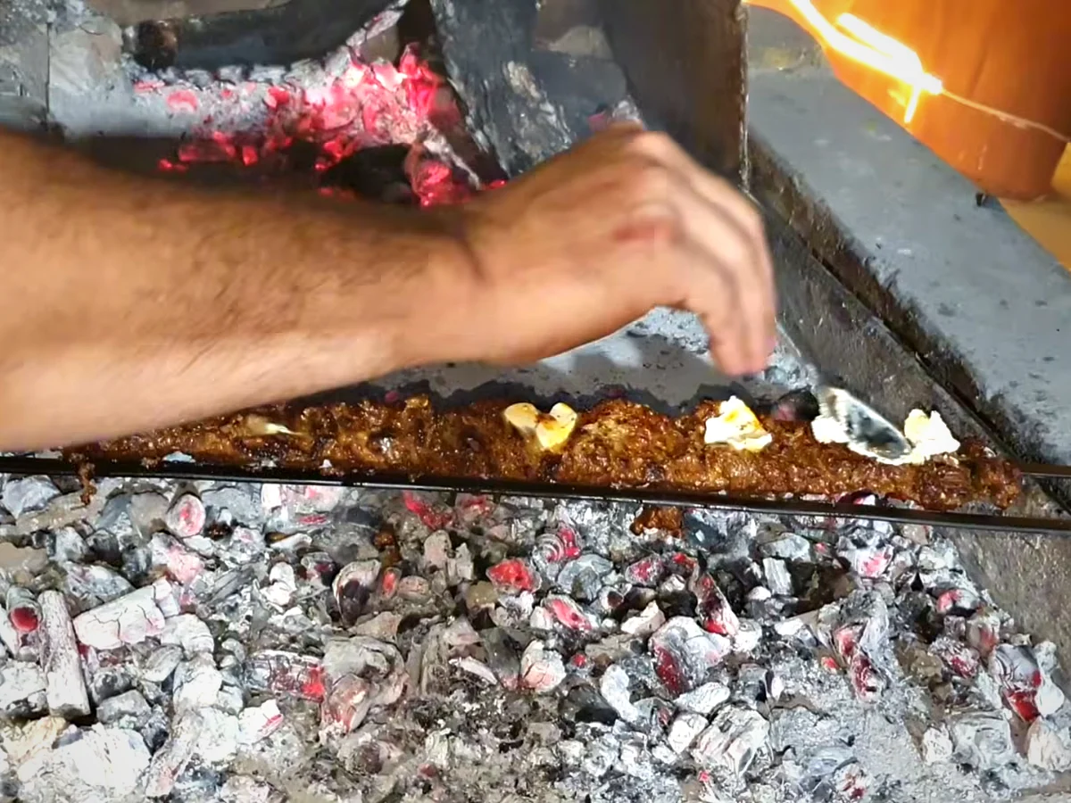 Butter being placed on bihari boti skewers on the grill