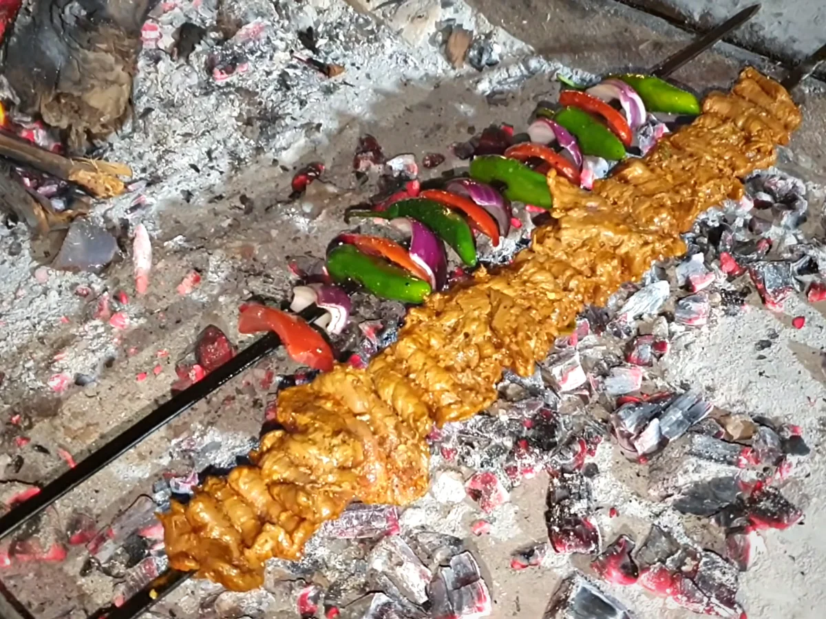 Bihari boti and vegetable skewers grilling over glowing coals
