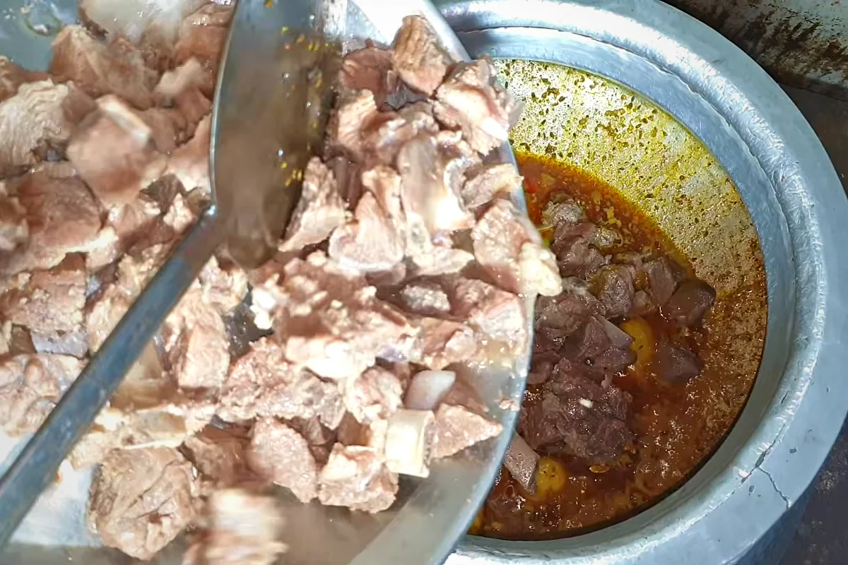 Boiled beef pieces being added to the biryani masala with potatoes