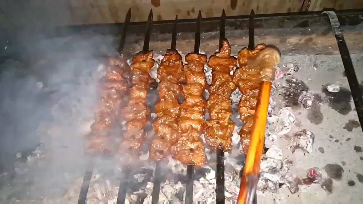 Brushing oil over beef Bihari kabab skewers on the coal grill