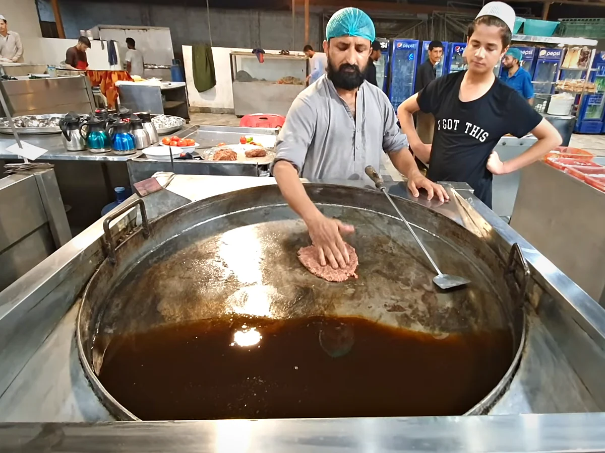 Chef sliding chapli kabab into a large karahi of hot oil