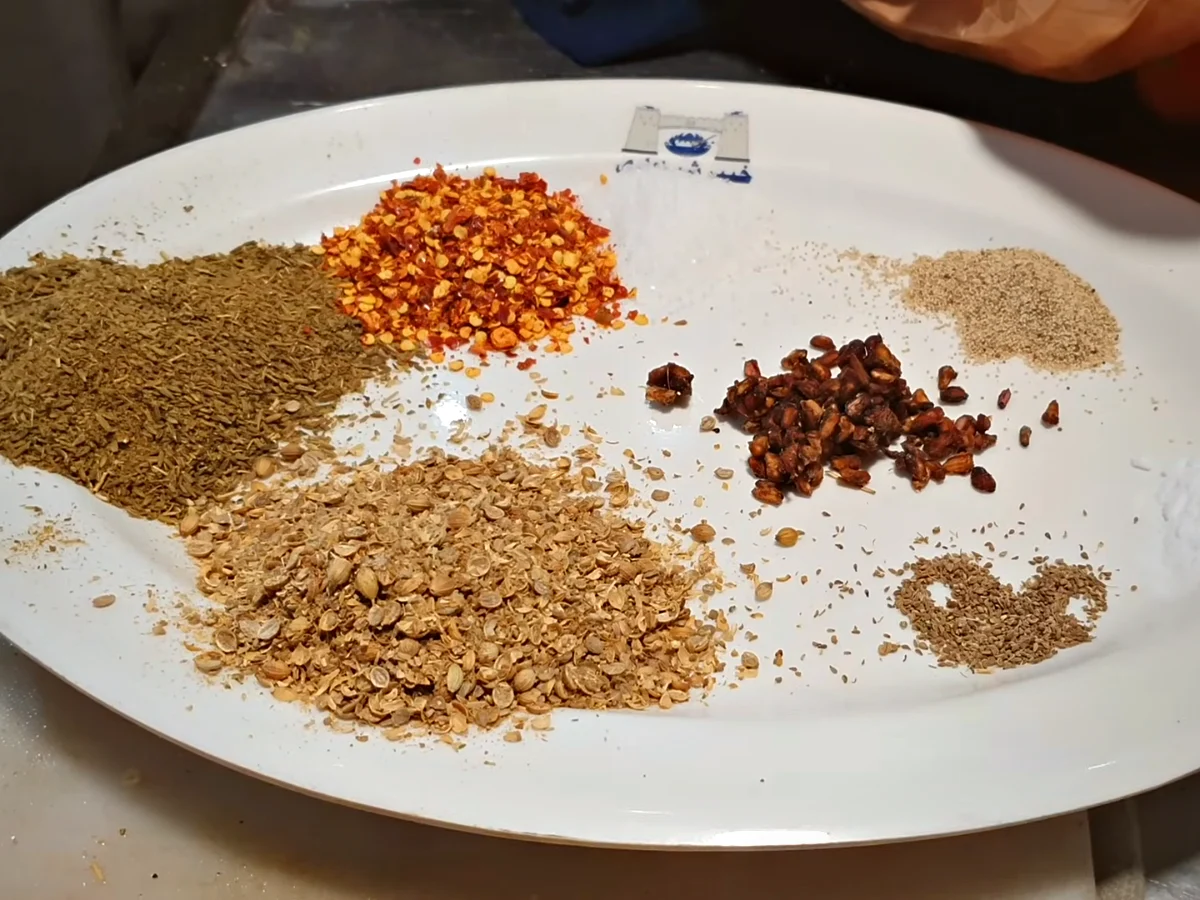 Chapli kabab spices on a plate: cumin, coriander, anardana, chilli flakes, carom and poppy seeds