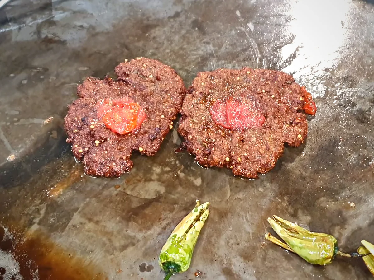 Fried chapli kababs topped with a soft tomato slice