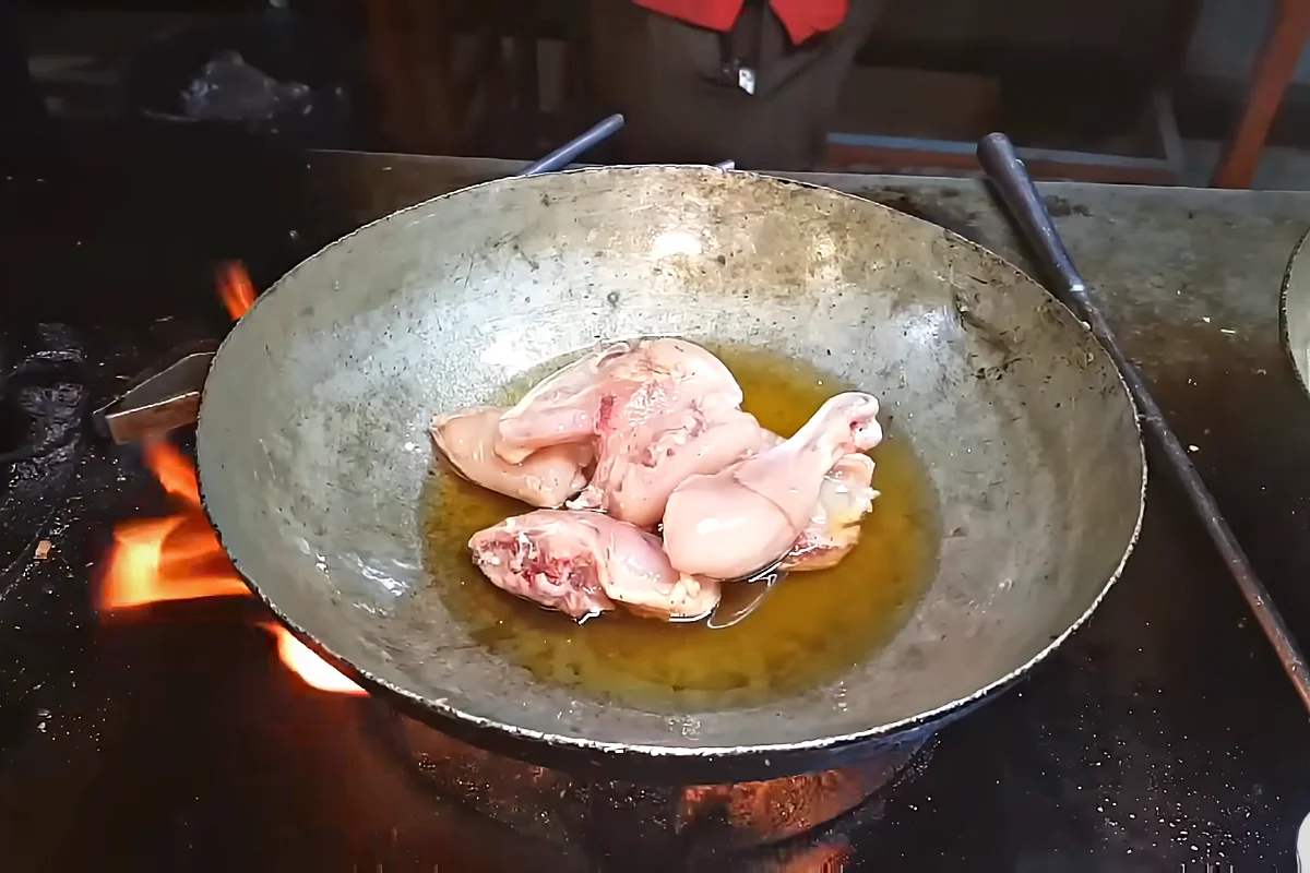 Chicken pieces going into hot oil in a street karahi