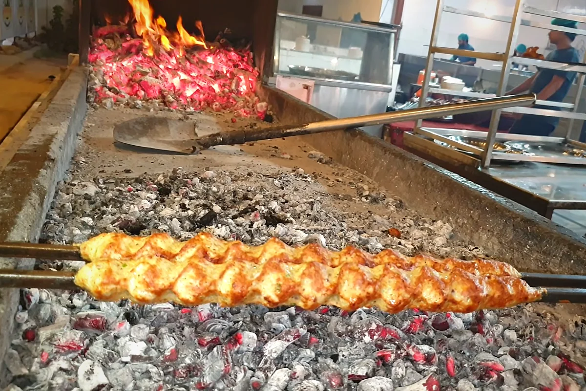 Chicken reshmi kabab skewers turning golden over hot coals