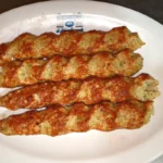 Four chicken reshmi kababs with a spiral pattern on a white plate
