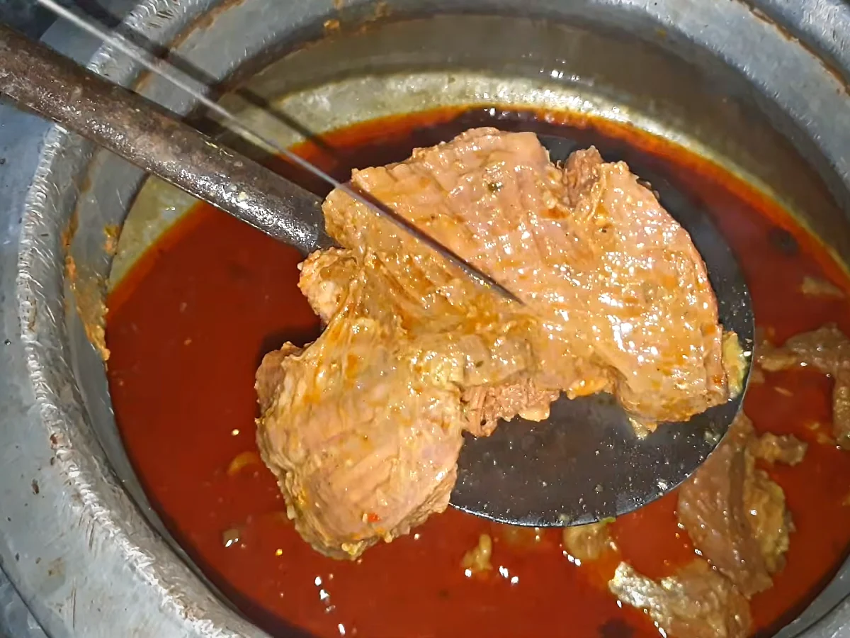 Cooked beef being lifted out of the red gravy for haleem