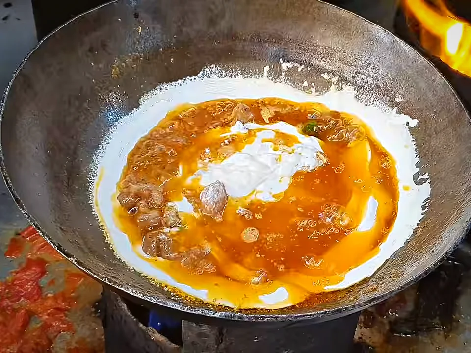Cream being added to mutton handi on a low flame