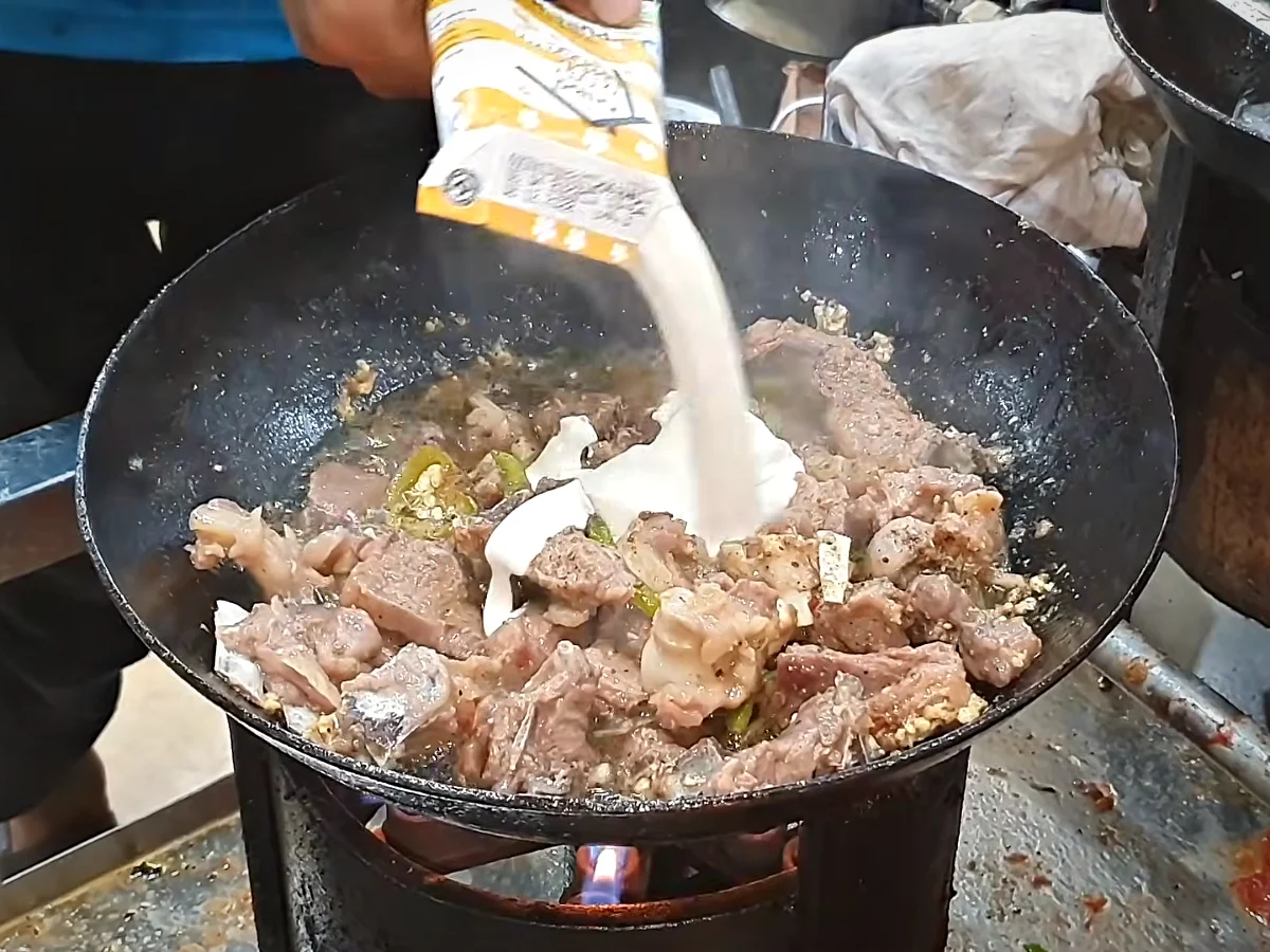 Cream being poured into white mutton karahi on low flame
