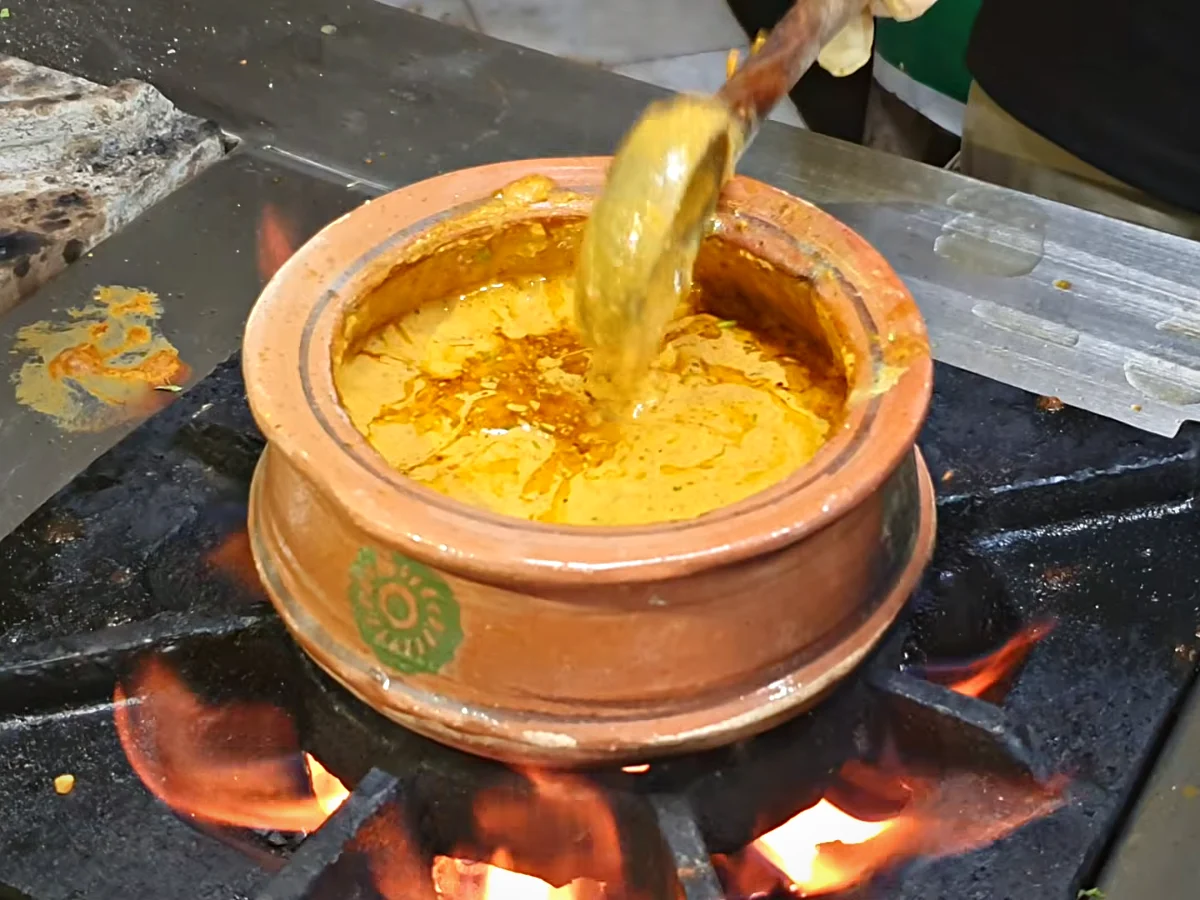 Ghee tadka being poured over dal makhani in a clay handi