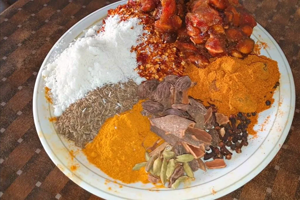 Plate of cumin, turmeric, red chilli flakes, dried plums, salt and whole spices for degi biryani