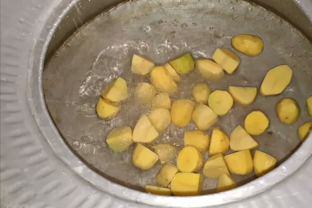 Potato pieces boiling in water in a large deg for degi chicken biryani