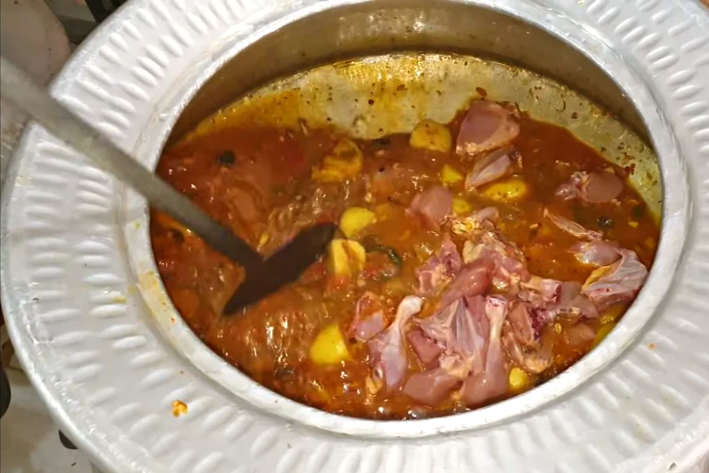Raw chicken pieces added to the potato and tomato masala in the deg