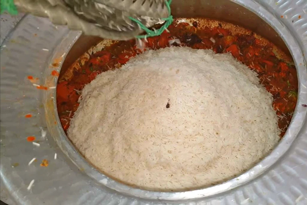 Par-boiled basmati rice piled over the chicken masala in the deg