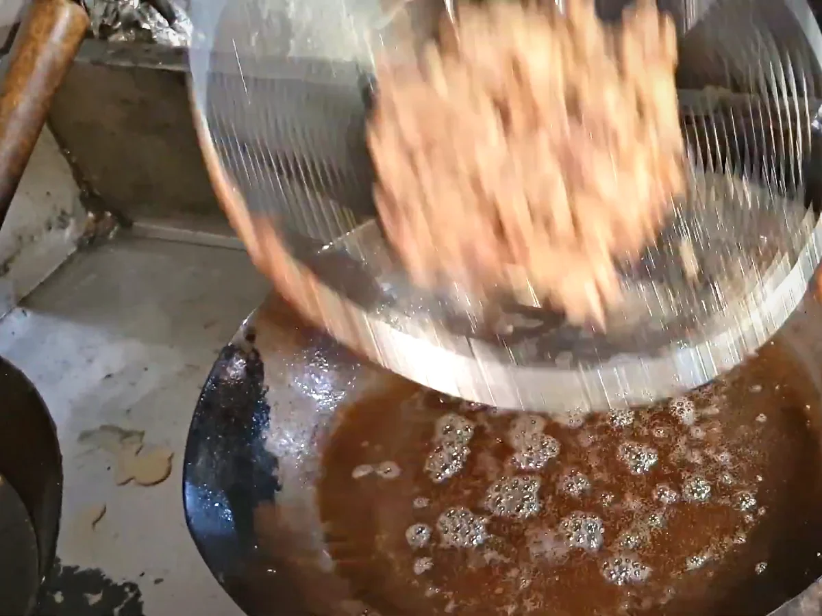 Fried beef strips being lifted out of the oil in a strainer