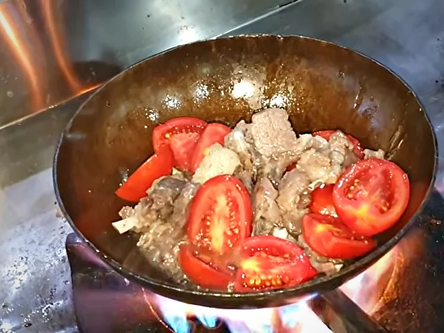 Halved tomatoes added to mutton chops in the karahi