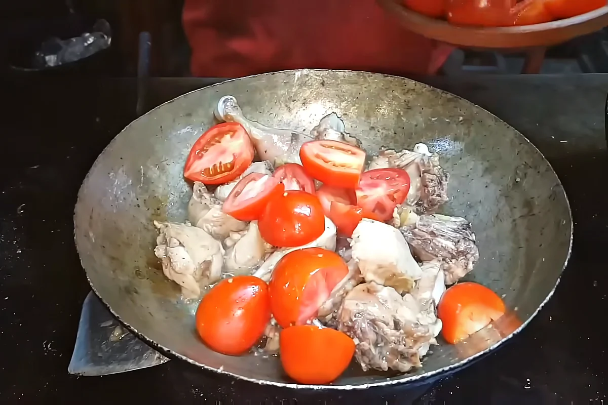 Halved tomatoes placed over chicken in a karahi