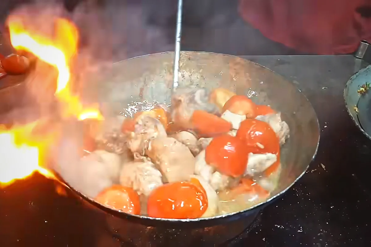 Flames rising around a karahi of chicken and tomatoes