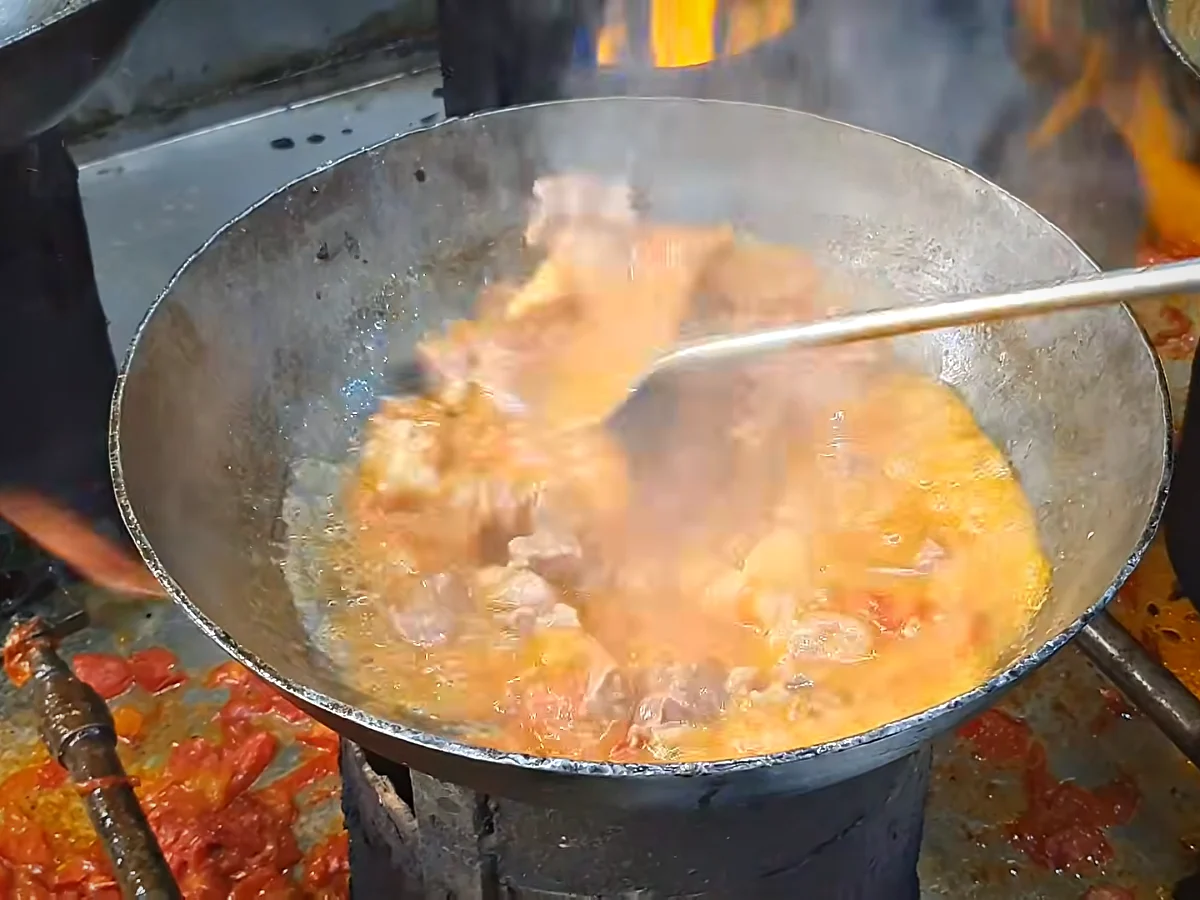 Softened tomatoes being peeled and mashed into the mutton