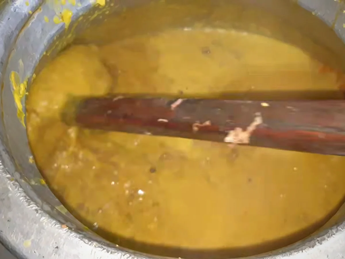 Beef and lentils being mixed with a wooden ghotna for haleem