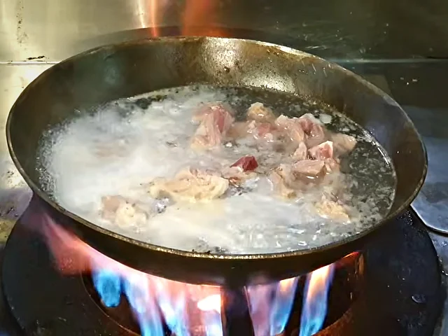 Mutton chops boiling in a karahi with scum on the surface