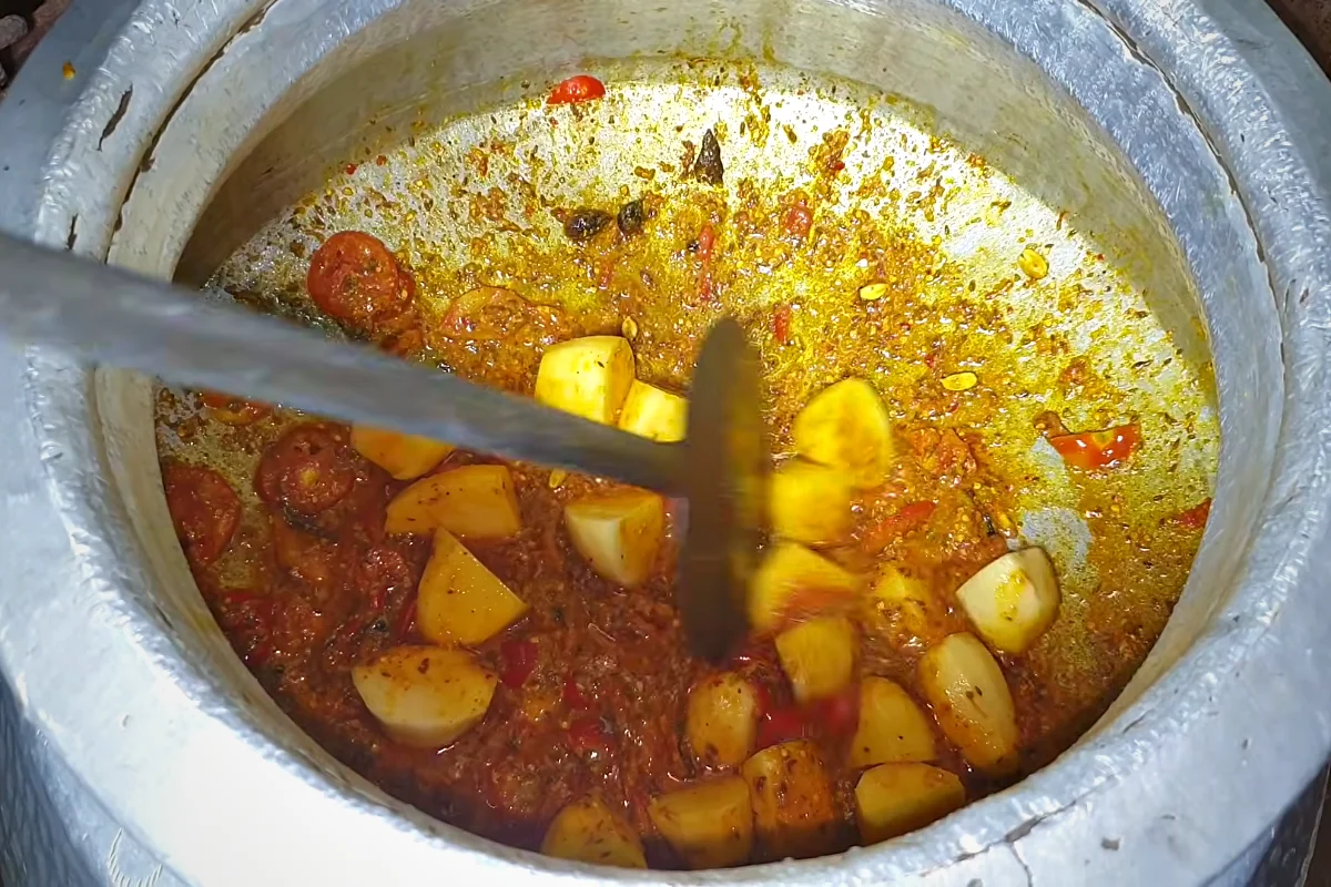 Potato pieces cooking in the red biryani masala in a large deg