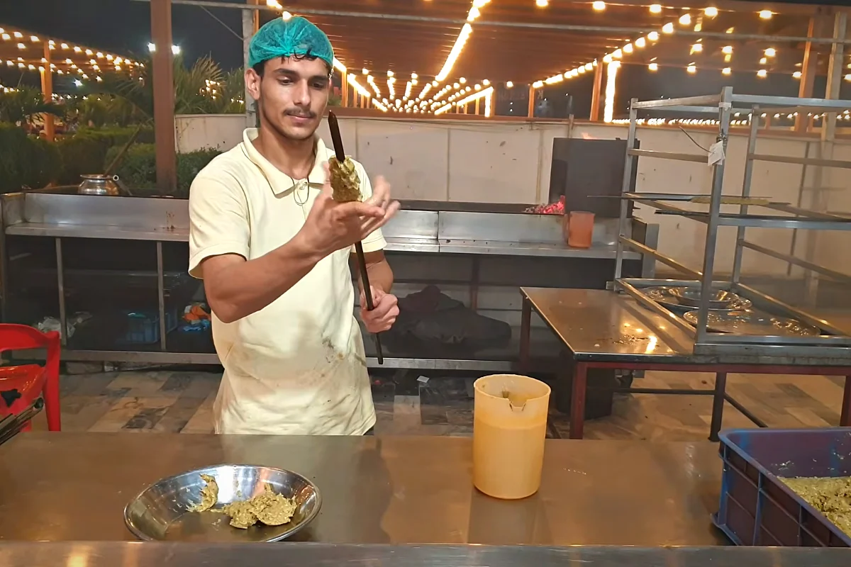Shaping minced chicken reshmi kabab onto a long skewer by hand