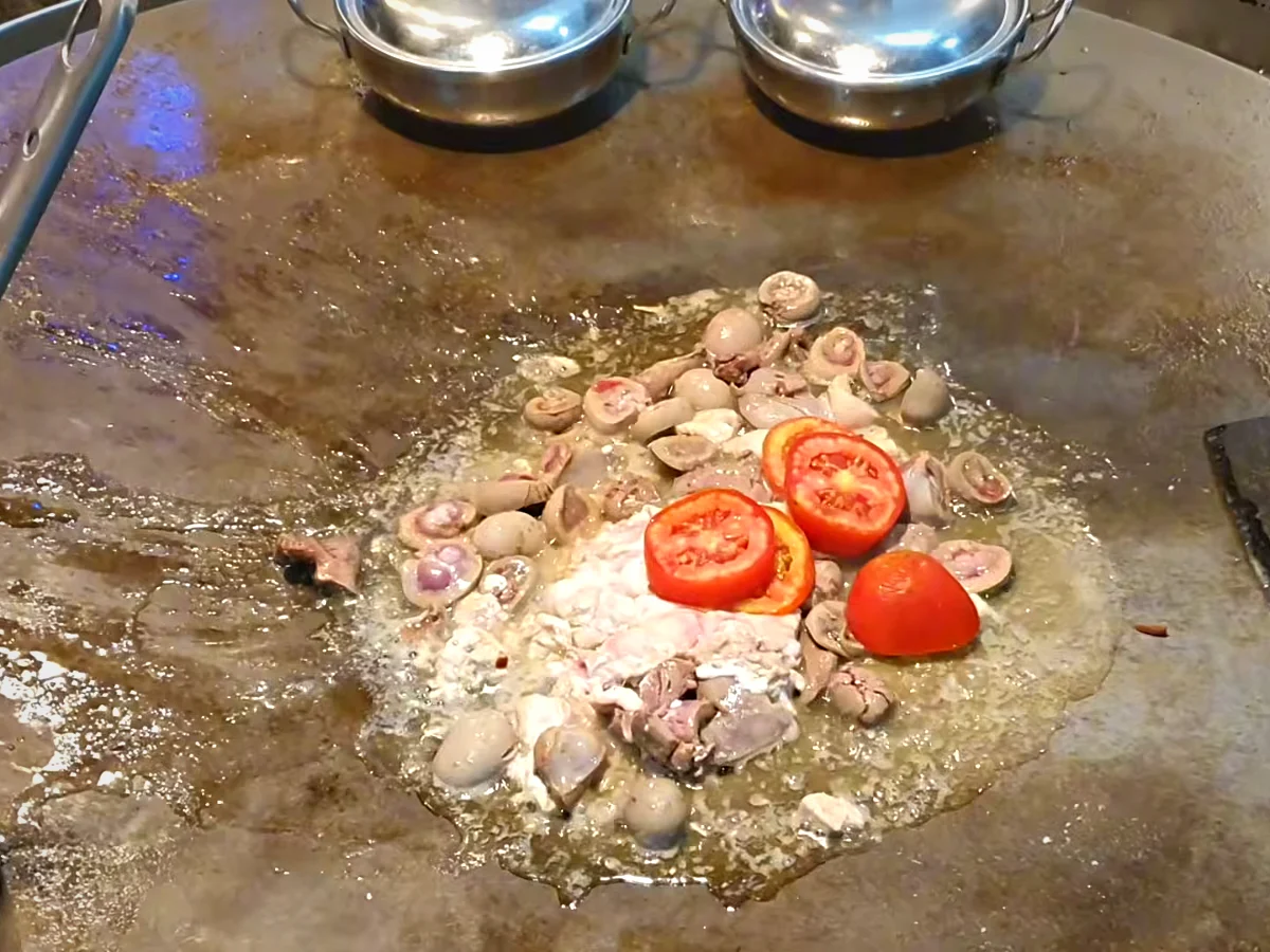 Halved tomatoes added to goat heart and kidneys on the tawa