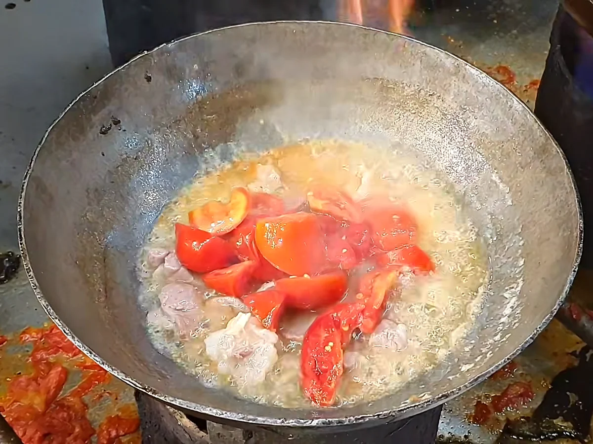 Whole tomatoes and ginger garlic paste added to cooked mutton in a handi
