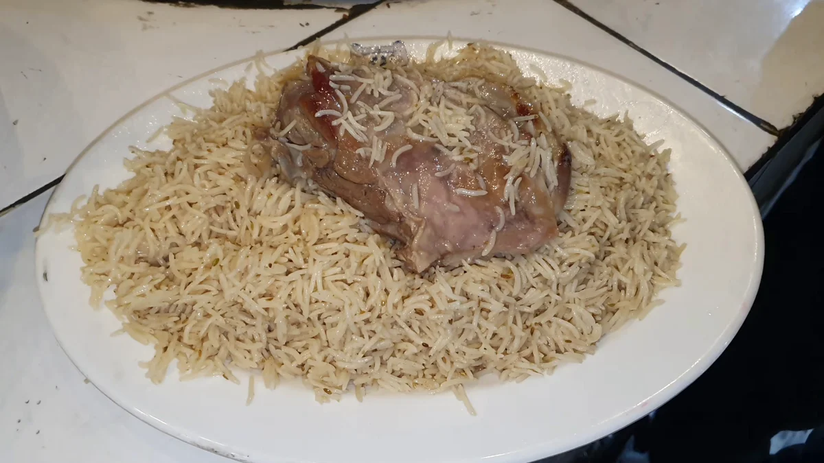 Afghani mutton pulao on a white platter with a large piece of mutton resting on golden rice