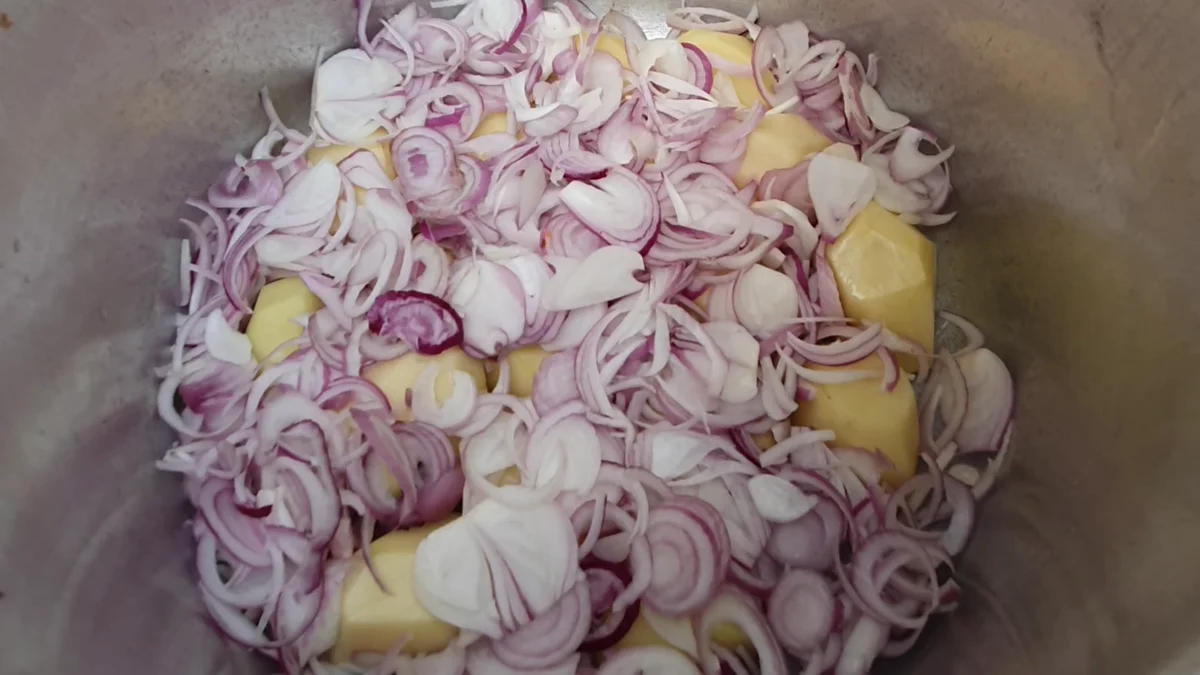 Sliced red onions piled in a pressure cooker at the start of the mutton yakhni