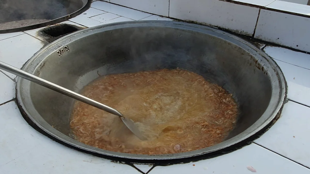 Golden-brown stock simmering in the large deg before the rice goes in