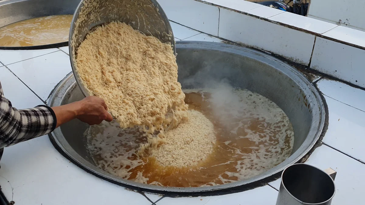 Rice being tipped from a tray into the stock in the deg