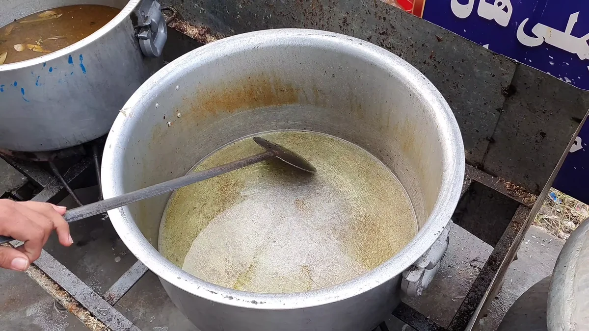 Large steel pot with the pulao base being stirred with a ladle
