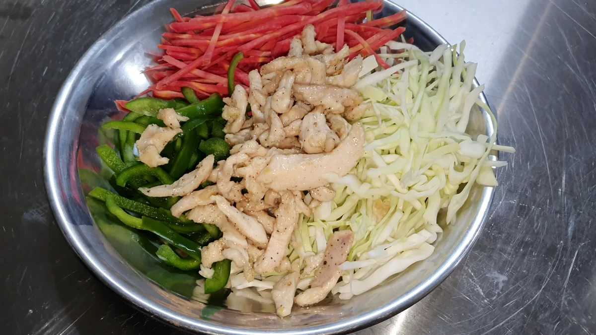 Chicken strips, cabbage, carrot and capsicum prepared in a steel bowl