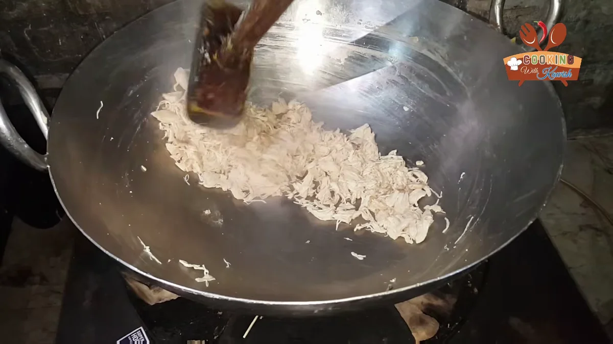 Boiled chicken being shredded in a wok