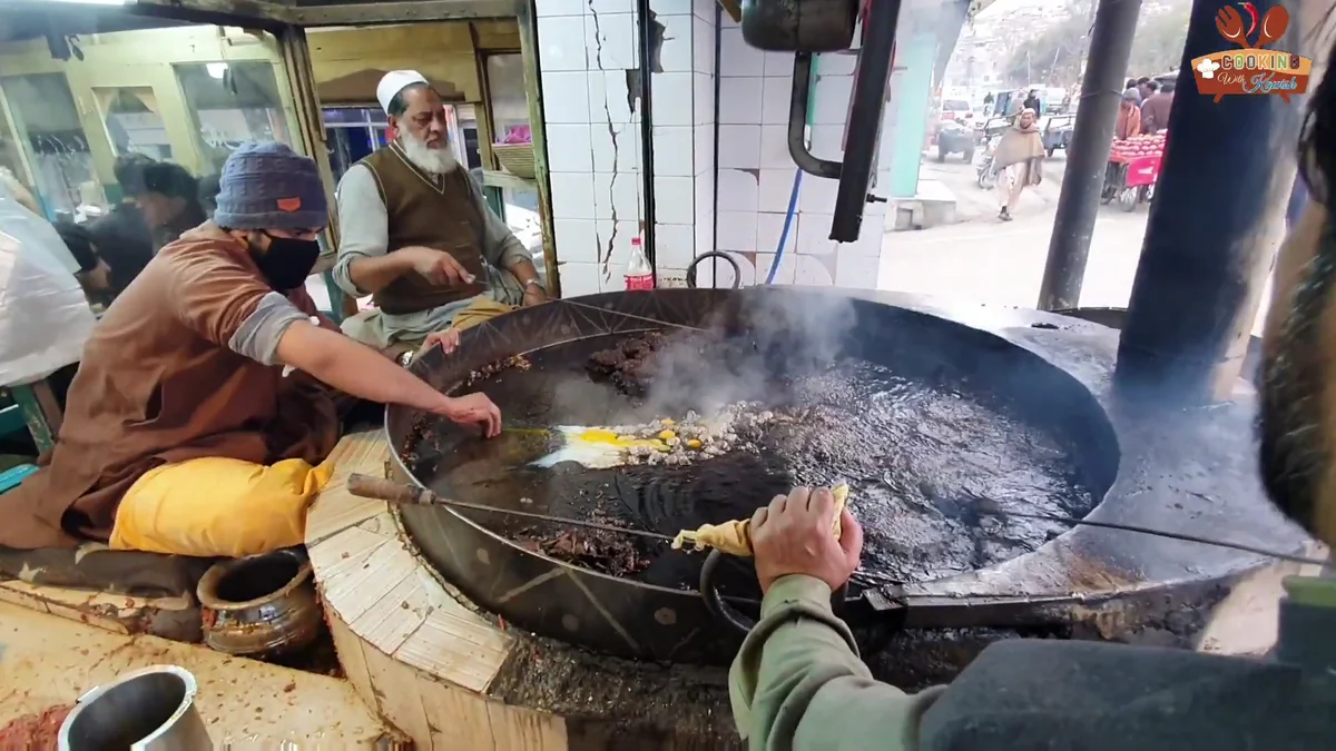 Chapli kababs frying in a very large pan over a wood fire