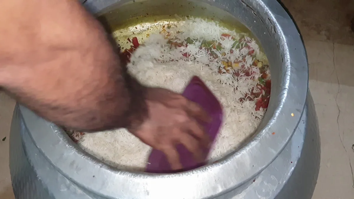 Boiled rice being spread over the biryani gravy
