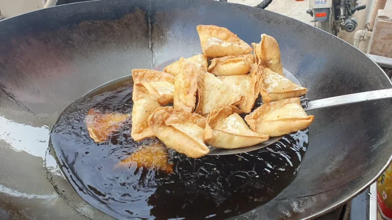 Golden aloo samosas lifted out of hot oil in a large wok