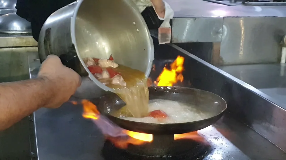 Pouring the pressure-cooked chicken into a wide karahi over the flame