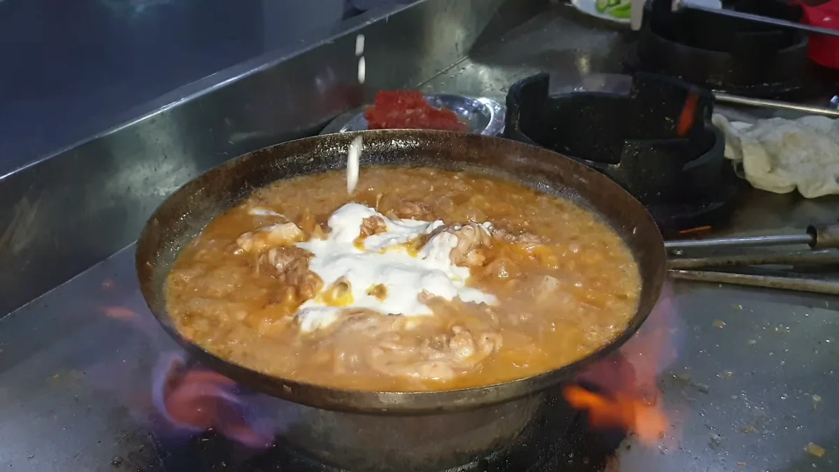 Yogurt being added to the chicken in the karahi