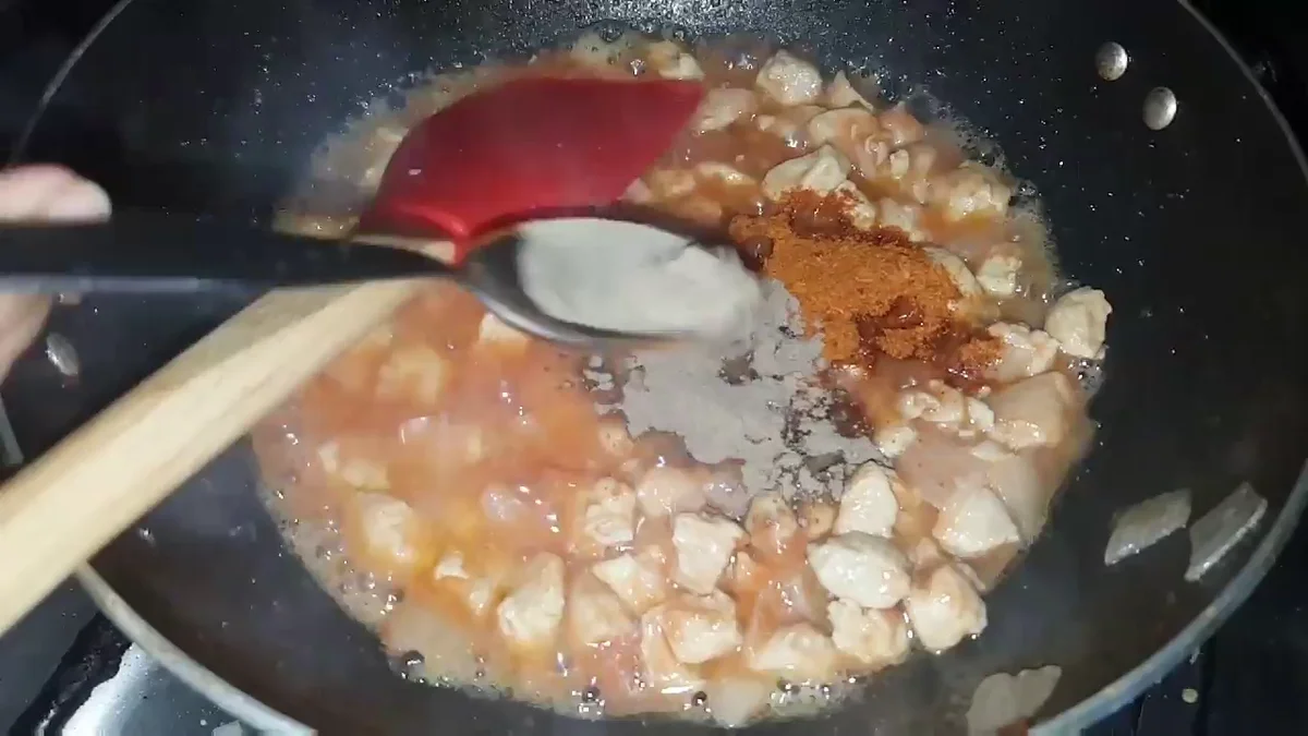 Red chilli powder and black pepper being added to the sauce