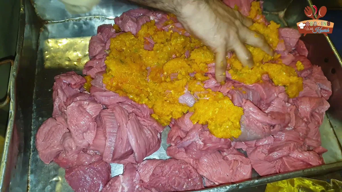 Thin beef strips in a large tray with an orange paste on top