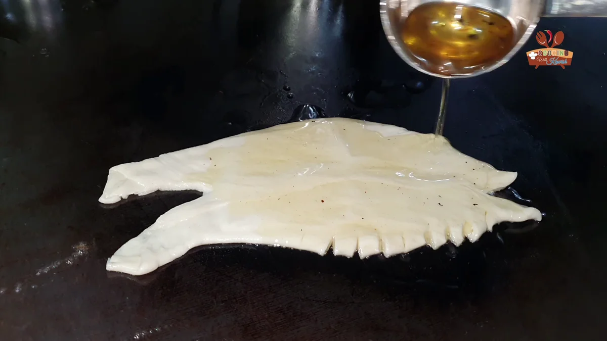 Ghee poured over the layered paratha on the tawa