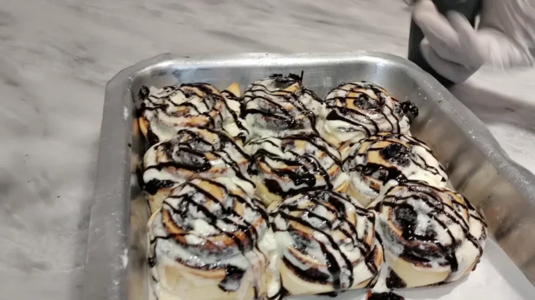 Tray of mini cinnamon rolls topped with icing and chocolate syrup