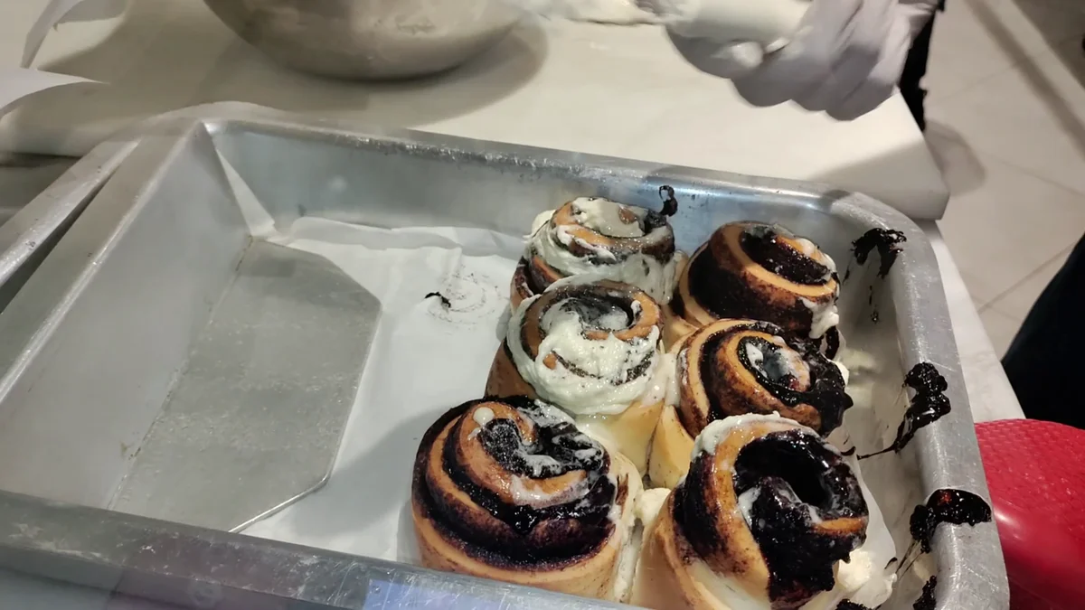 White icing being spread over the baked rolls