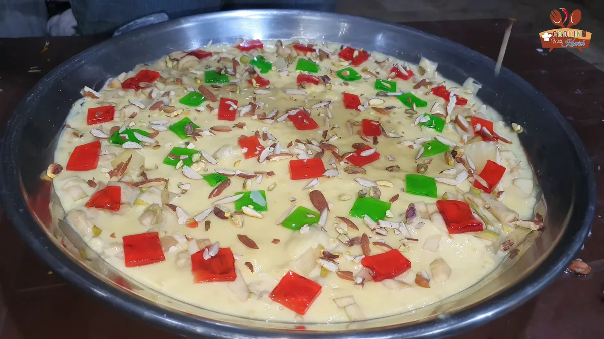Fruit custard trifle topped with red and green jelly cubes and chopped nuts