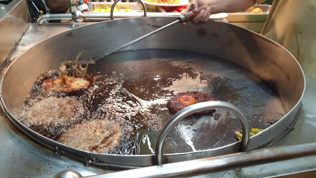 Chapli kababs frying with a tomato slice on top