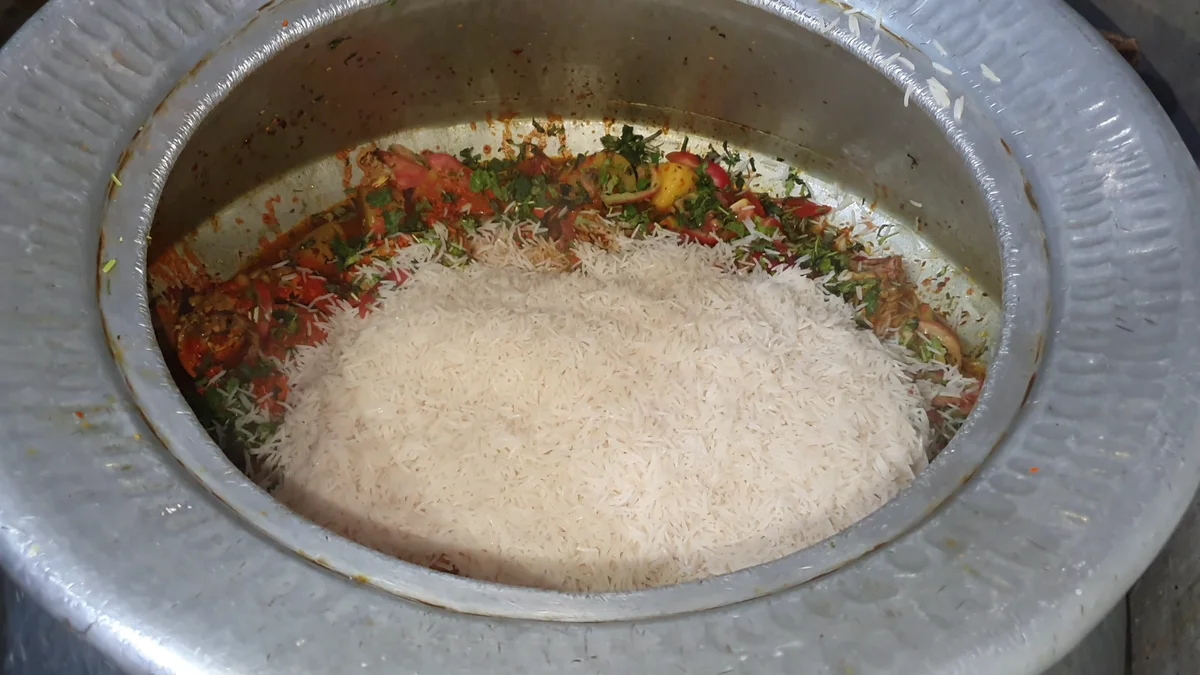 Par-boiled rice spread over the chicken gravy in the deg